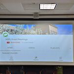 Thumbnail: Large format projector screen demonstrated by showing the public library’s YouTube account’s Board Meetings’ homepage.