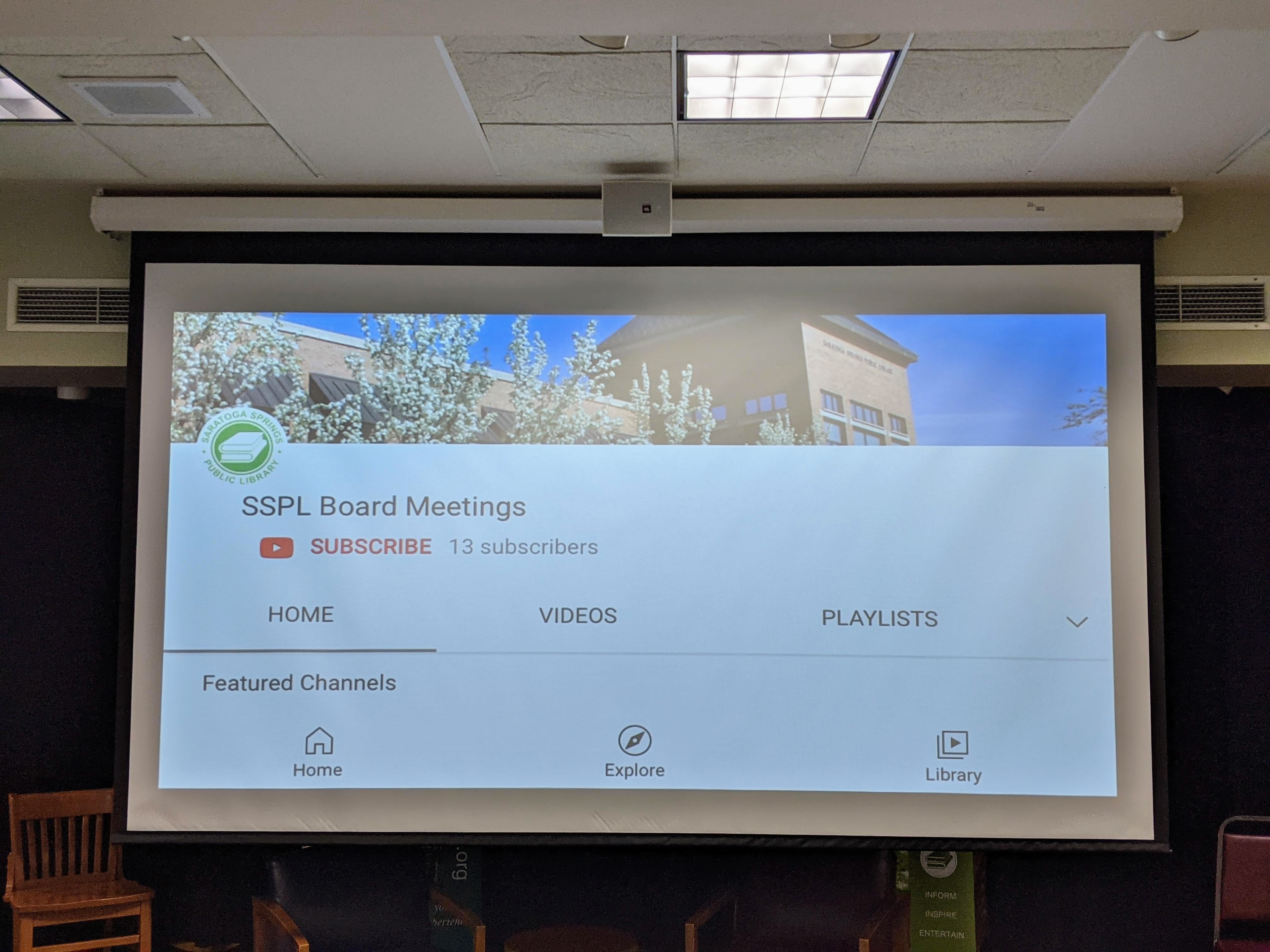 Large format projector screen demonstrated by showing the public library’s YouTube account’s Board Meetings’ homepage.