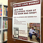 Thumbnail: A paper sign taped to a shelf looking for volunteers to help work at the book shop.