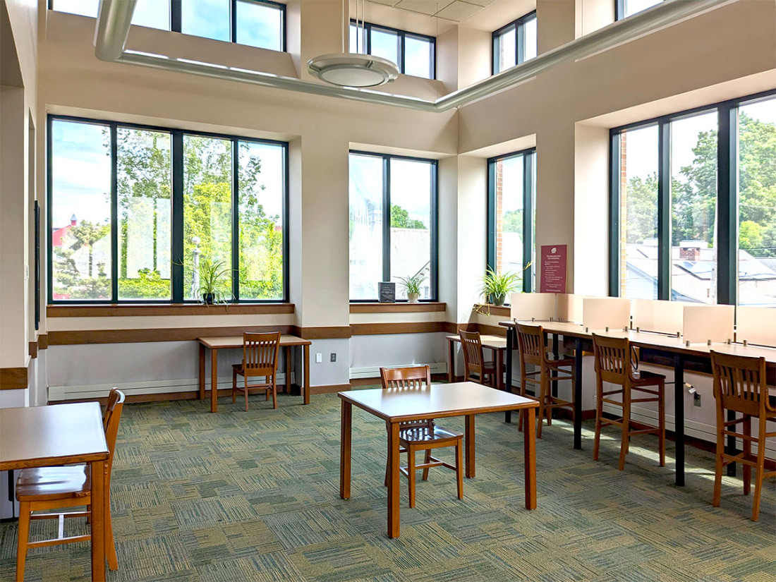 Tables with chairs around a room’s perimeter, against the walls. One lone table and chair in the center of the floor. Many windows cover the majority of the walls.