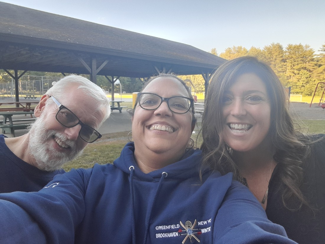 3 people smiling at the camera.  Man on left in black shirt with glasses.  Woman in middle with blue sweatshirt and glasses.  Woman on right in black shirt