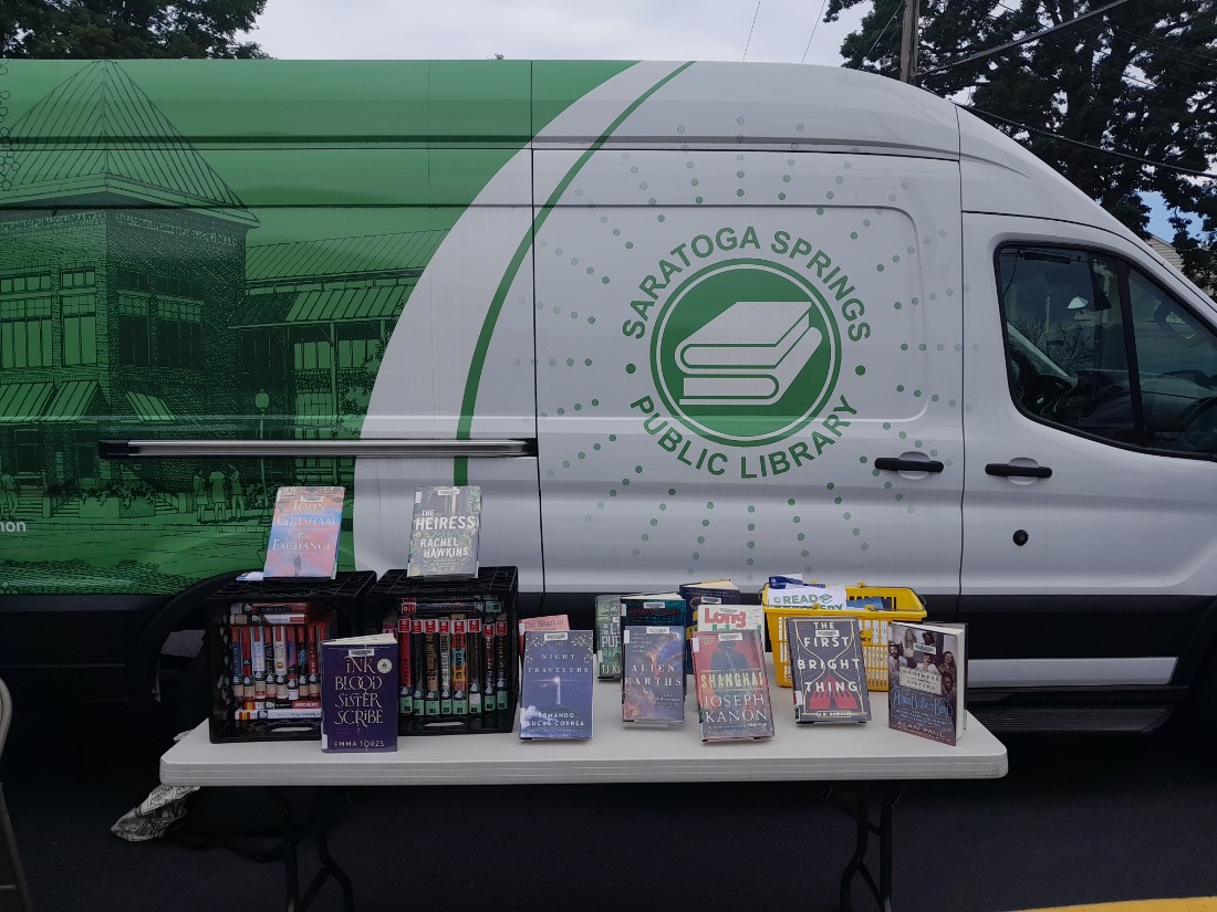 A panel van, decorated with the library’s colors of green and white showcasing a two-tone photo depicting the library all in green on the back half and the library logo in green on white on the front.