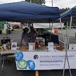 Thumbnail: Two staff members from Saratoga Hospital under a blue tent standing behind a table with information and a white Saratoga Hospital banner hanging from front of table