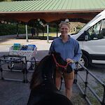 Thumbnail: a woman in a blue shirt standing outside with a brown miniature horse, pavilion with green roof in background